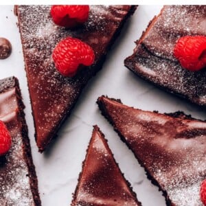 Slices of flourless chocolate cake topped with powdered sugar and raspperries.