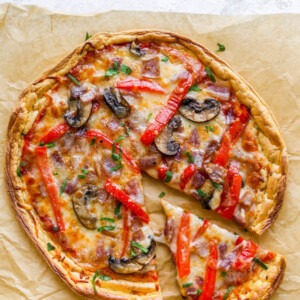 An overhead view of cloud bread pizza on a sheet of brown parchment paper. A slice has been cut and slightly removed from the pizza.