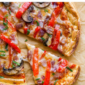 A closeup of a slice of cloud bread pizza removed from a whole pizza on a sheet of brown parchment paper.