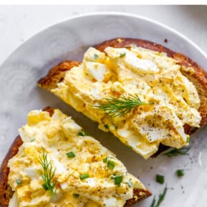 A plate with a slice of bread topped with healthy egg salad. The slice has been cut in half.