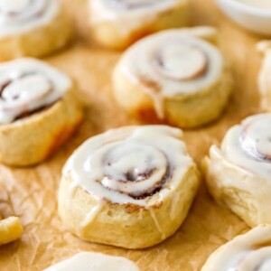 Iced cinnamon rolls on a sheet of parchment paper.