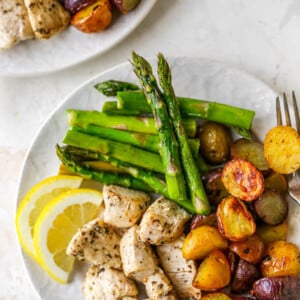 A plate with asparagus, chicken, potatoes and lemon wedges.