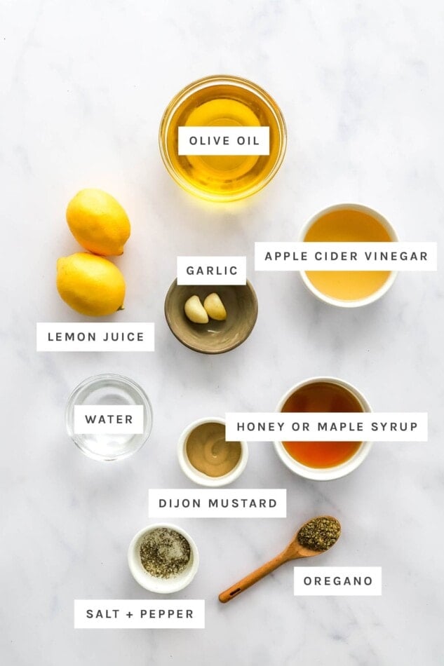 Ingredients measured out to make lemon dressing: olive oil, lemon juice, apple cider vinegar, garlic, water, honey or maple syrup, dijon mustard, oregano, salt and pepper.