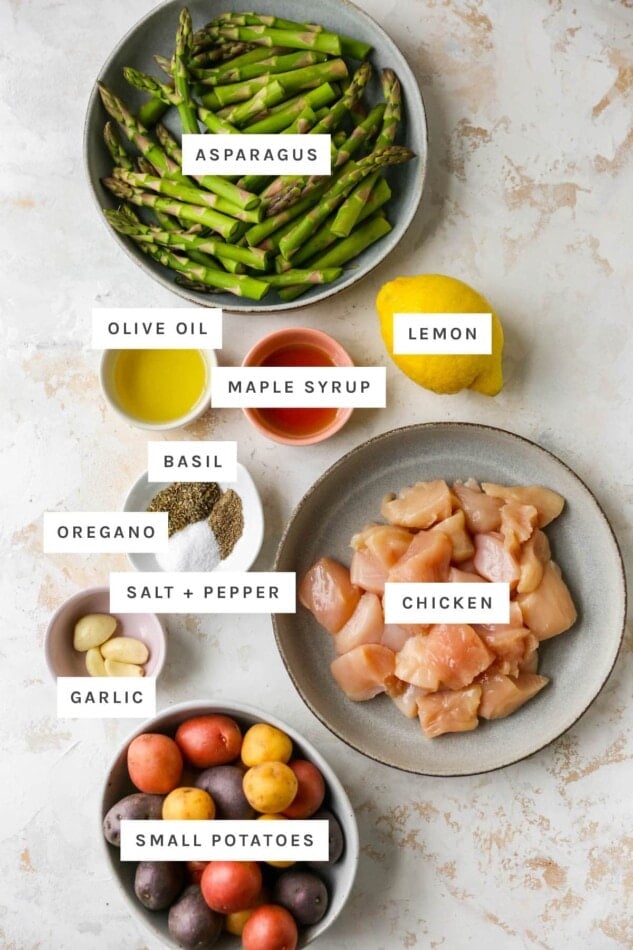 Ingredients measured out to make a lemon garlic sheet pan meal: asparagus, olive oil, maple syrup, lemon, basil, oregano, salt, pepper, chicken, garlic and small potatoes.