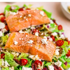 A serving platter with mediterranean salad topped with two filets of salmon.