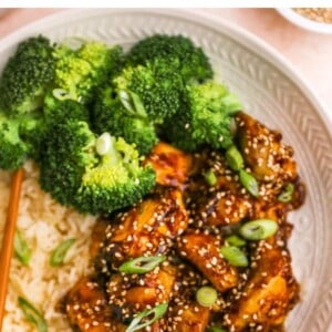 An overhead closeup view of sesame chicken on a plate. Rice and broccoli are also on the plate.