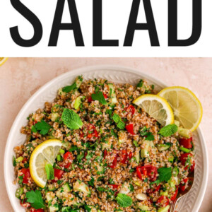 A serving platter with tabbouleh salad topped with fresh mint and lemon slices. A spoon rests on the platter.