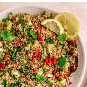 A serving platter with tabbouleh salad topped with fresh mint and lemon slices. A spoon rests on the platter.