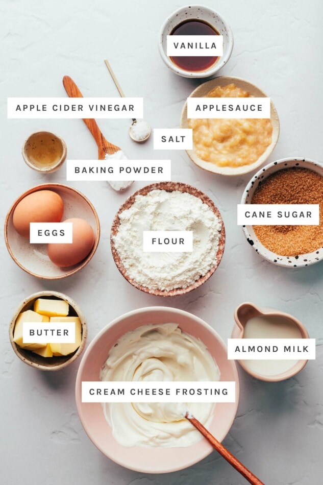 Ingredients measured out to make vanilla cupcakes: vanilla, applesauce, salt, apple cider vinegar, baking powder, cane sugar, flour, eggs, butter, almond milk and cream cheese frosting.