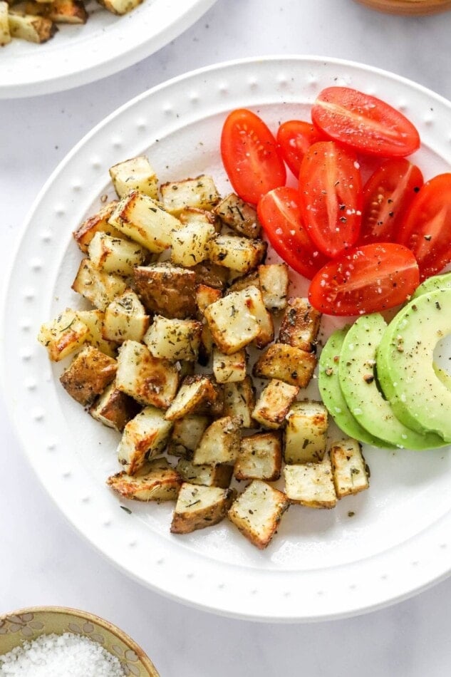 An overhead view of a plate containing air fryer breakfast potatoes alongside tomato and avocado slices.