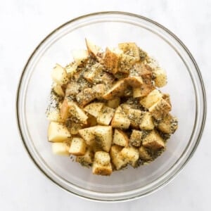 Evenly diced potatoes in a bowl, tossed with herbes de provence, sea salt, ground pepper, garlic powder and onion powder.