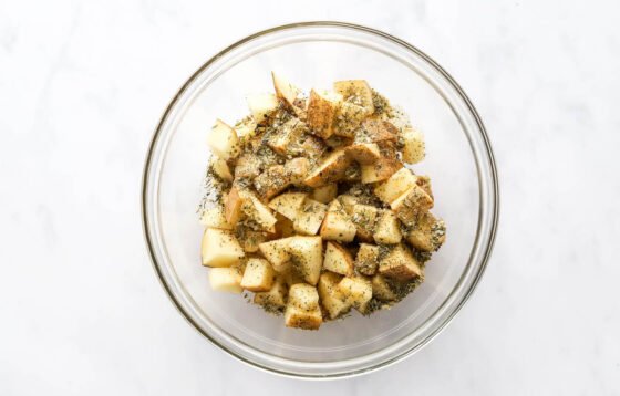 Evenly diced potatoes in a bowl, tossed with herbes de provence, sea salt, ground pepper, garlic powder and onion powder.