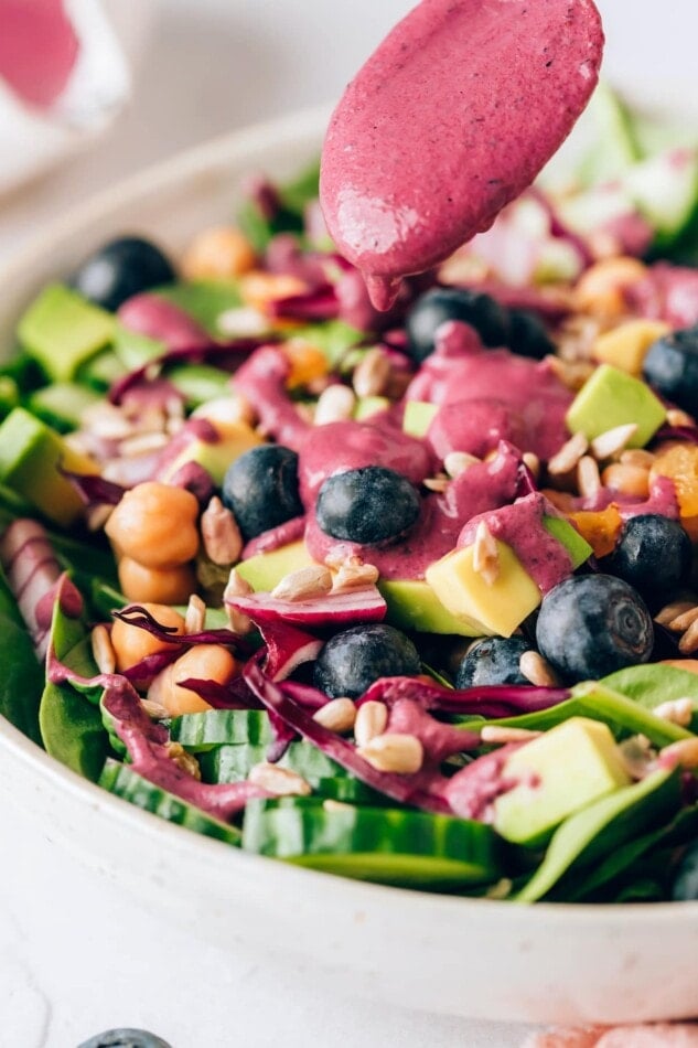 Drizzling blueberry tahini dressing on a spinach blueberry salad.