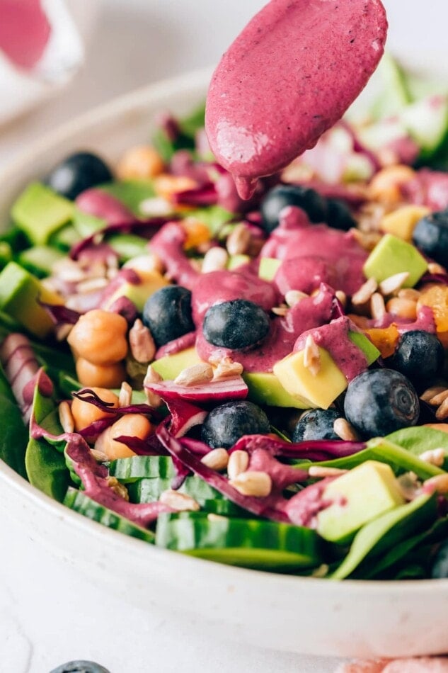 Drizzling blueberry tahini dressing on a spinach blueberry salad.