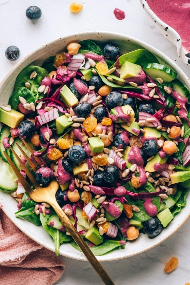 A closeup of a bowl containing spinach blueberry salad. A fork rests in the bowl.
