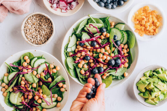 Adding blueberries and other toppings to the spinach in a bowl.