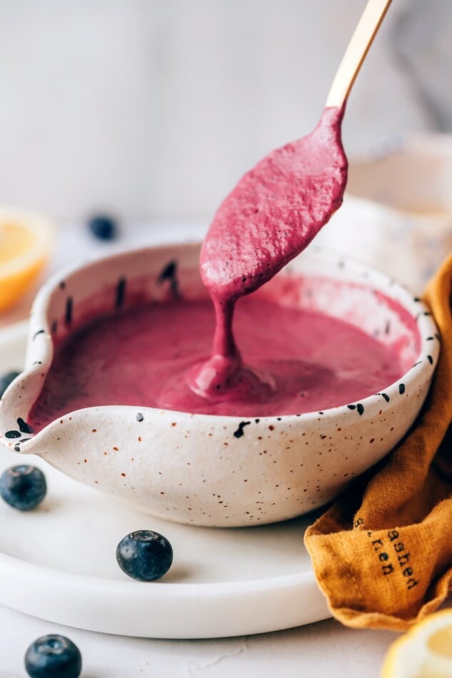 A small serving dish with blueberry tahini dressing. A spoon is dripping the dressing back into the dish.