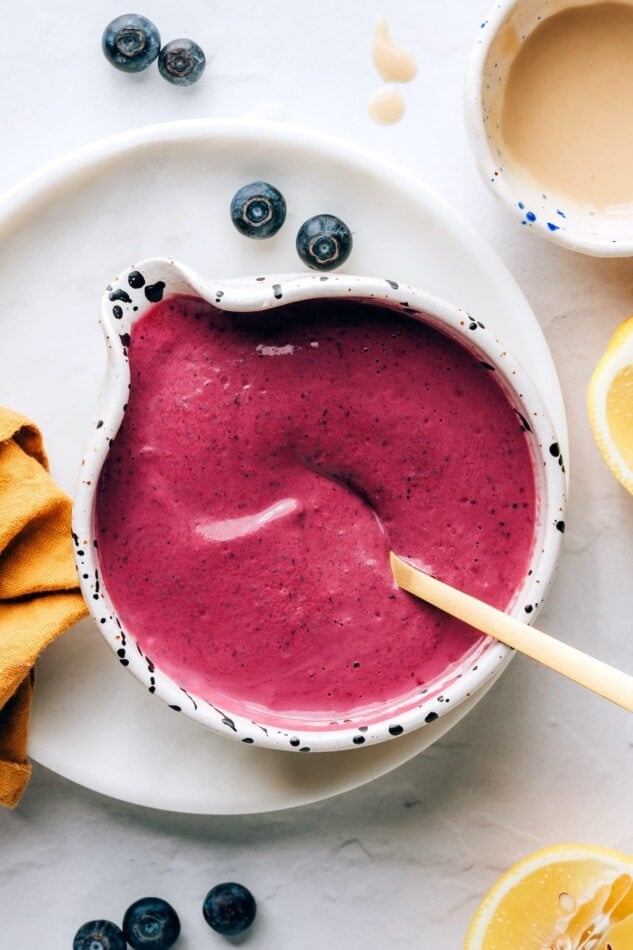 An overhead view of a small serving dish containing blueberry tahini dressing. A spoon rests in the dish.