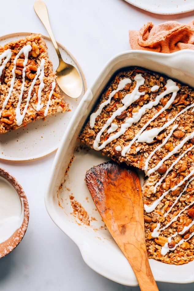 A baking dish containing carrot cake baked oatmeal. A plate with a slice is next to the dish.