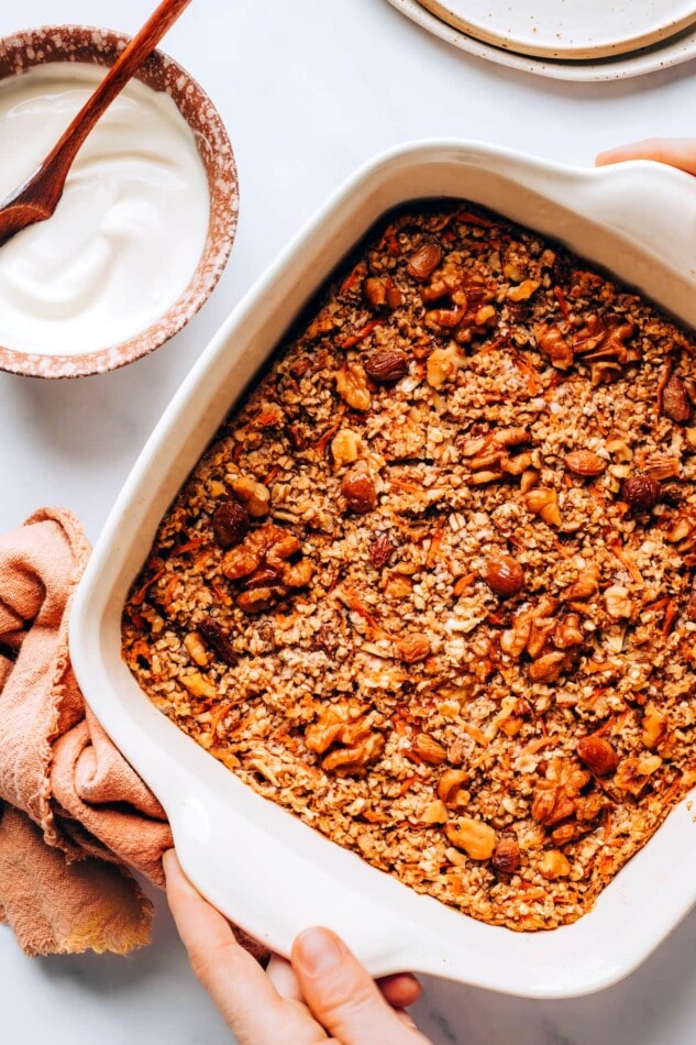 Carrot cake baked oatmeal in a baking dish. A small bowl of glaze in next to the dish.