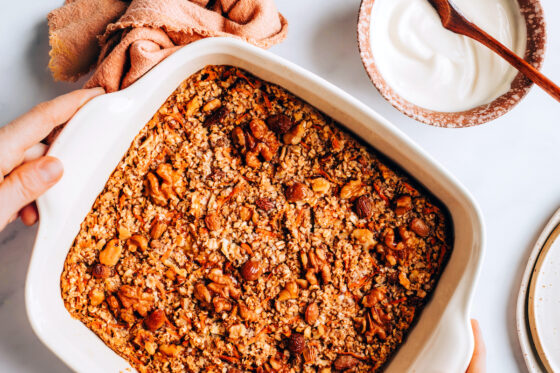 Carrot cake baked oatmeal in a baking dish. A small bowl of glaze in next to the dish.