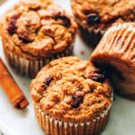 An angled photo of 4 carrot raisin muffins on a plate. One of the muffins is resting on it's side.