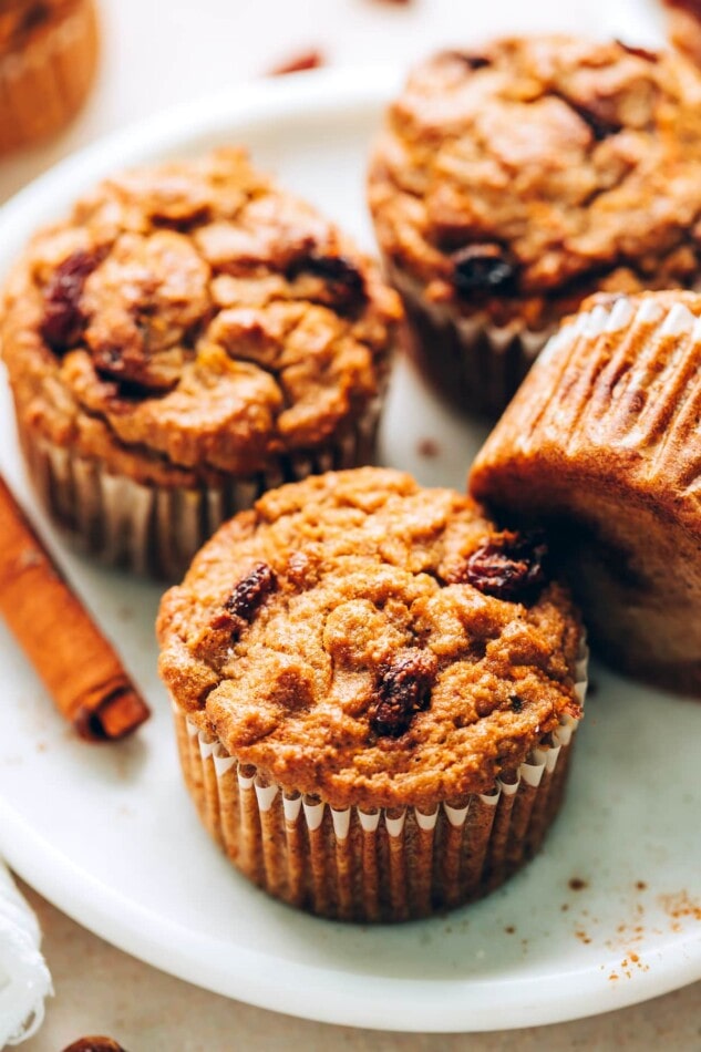 An angled photo of 4 carrot raisin muffins on a plate. One of the muffins is resting on it's side.