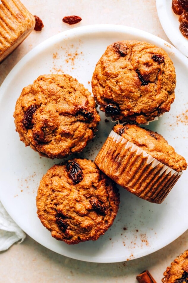 Overhead photo of 4 carrot raisin muffins on a plate. One of the muffins is resting on its side.