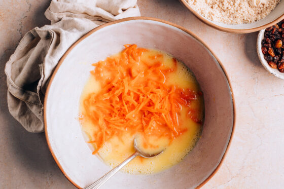 Eggs, almond milk, coconut oil, honey and coconut sugar mixed together in a bowl. Grated carrots have been added to the bowl.