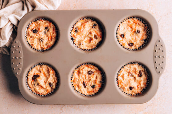 Muffin batter distributed between a 6 muffin tin lined with paper liners.