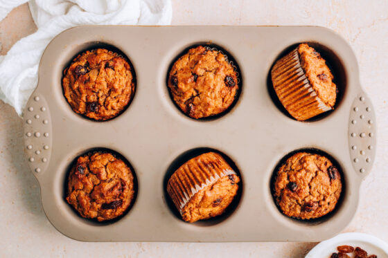 Six carrot raisin muffins in a muffin tin wrapped in paper liners.