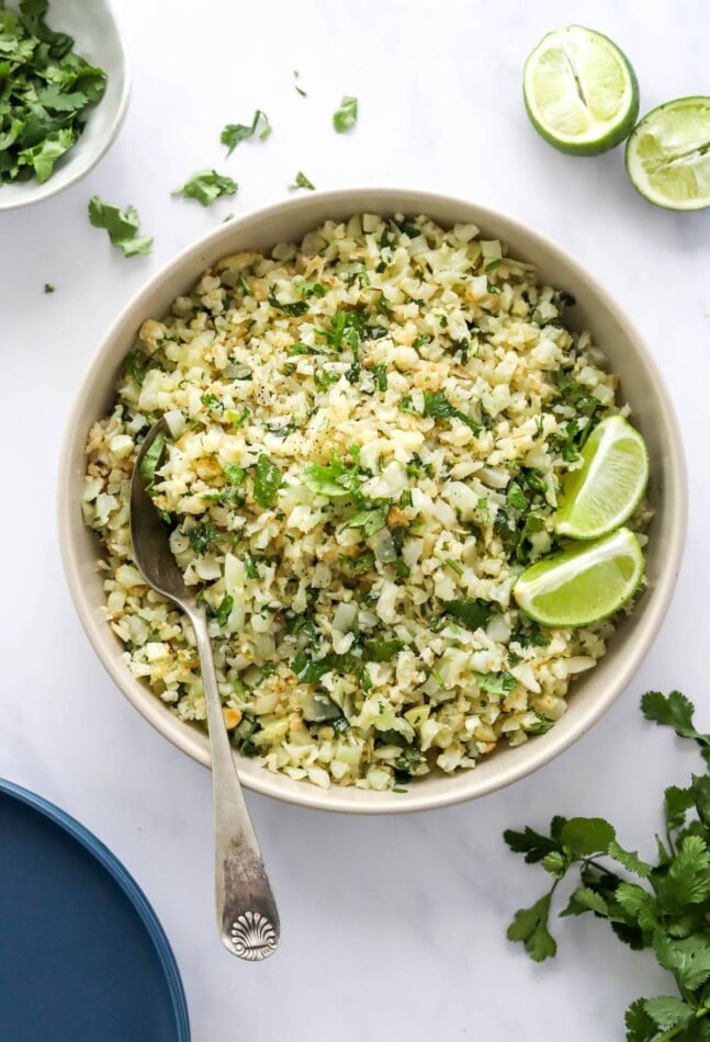 Looking down at a serving bowl containing cilantro lime cauliflower rice. A spoon rests in the bowl.