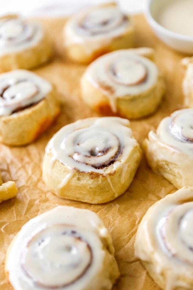 Iced cinnamon rolls on a sheet of parchment paper.