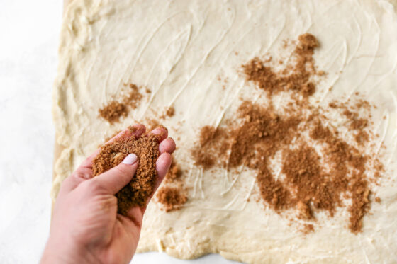 Cinnamon sugar mixture being spread across the top of the rectangle of dough.