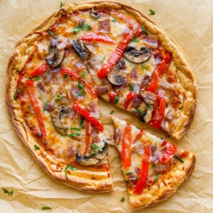 An overhead view of cloud bread pizza on a sheet of brown parchment paper. A slice has been cut and slightly removed from the pizza.