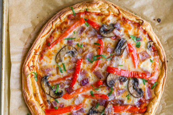 Close up of baked cloud bread pizza on baking sheet lined with brown parchment paper.