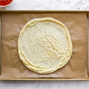 Baked egg white mixture pizza crust on a baking sheet lined with brown parchment paper.