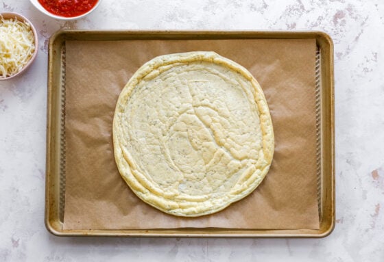 Baked egg white mixture pizza crust on a baking sheet lined with brown parchment paper.