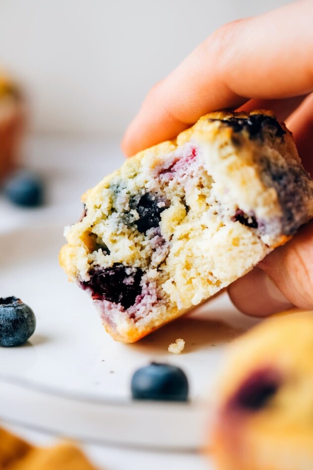 A hand holding a coconut flour muffin with a bite removed.