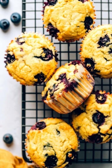 An overhead view of coconut flour muffins arranged on a wire cooling rack. One muffin is turned on its side.