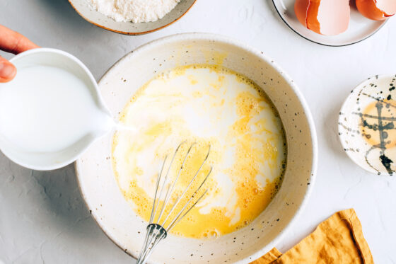 A medium mixing bowl with eggs, coconut milk, maple syrup and vanilla extract.