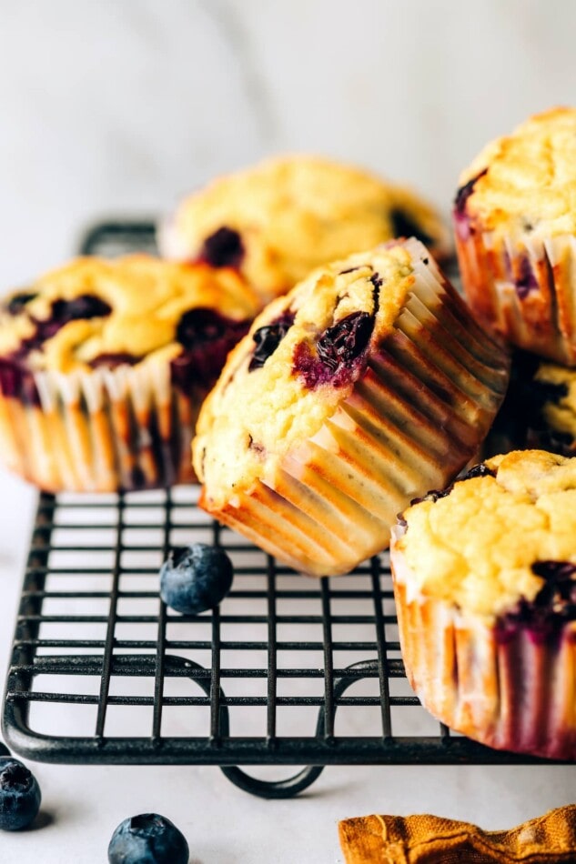 Coconut flour muffins on a wire cooling rack. The center muffin is angled on it's side, resting against other muffins.