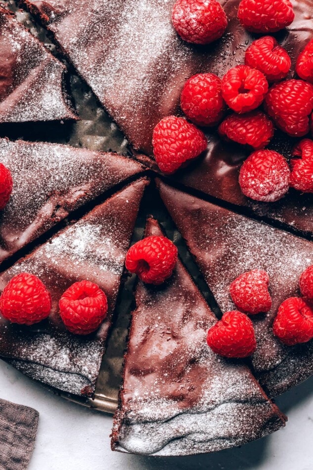 A closeup view of flourless chocolate cake sprinkled with powdered sugar and topped with raspberries.
