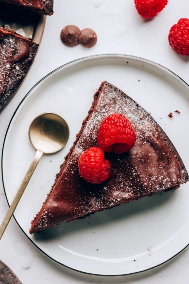 A slice of flourless chocolate cake on a white plate with a dessert spoon.