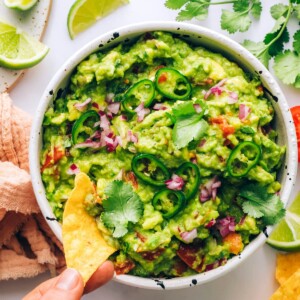 A chip scooping some guacamole out of a bowl.