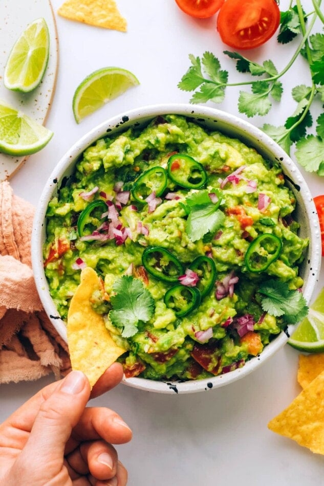 A chip scooping some guacamole out of a bowl.