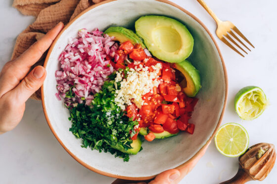 Avocado halves, tomato, red onion, cilantro, garlic and lime juice in a bowl.