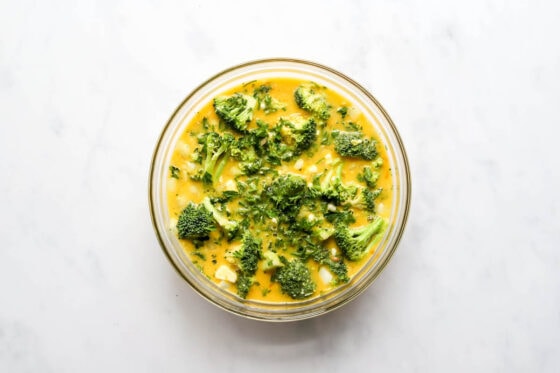 Eggs, almond milk, broccoli florets, cottage cheese, feta cheese, onion, parsley, garlic, salt and pepper in a bowl mixed together.