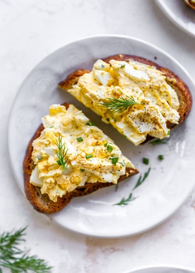 A plate with a slice of bread topped with healthy egg salad. The slice has been cut in half.