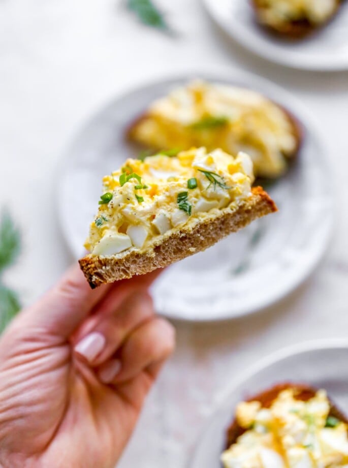 A hand holding up a piece of bread topped with healthy egg salad.